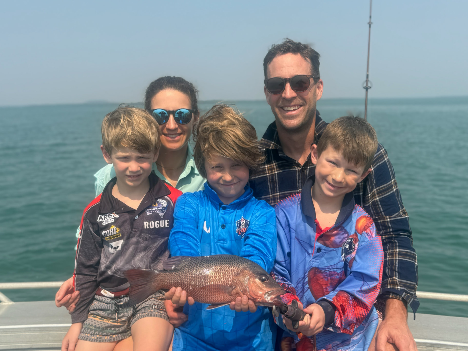 Family of anglers smiling and holding a mangrove jack on the boat