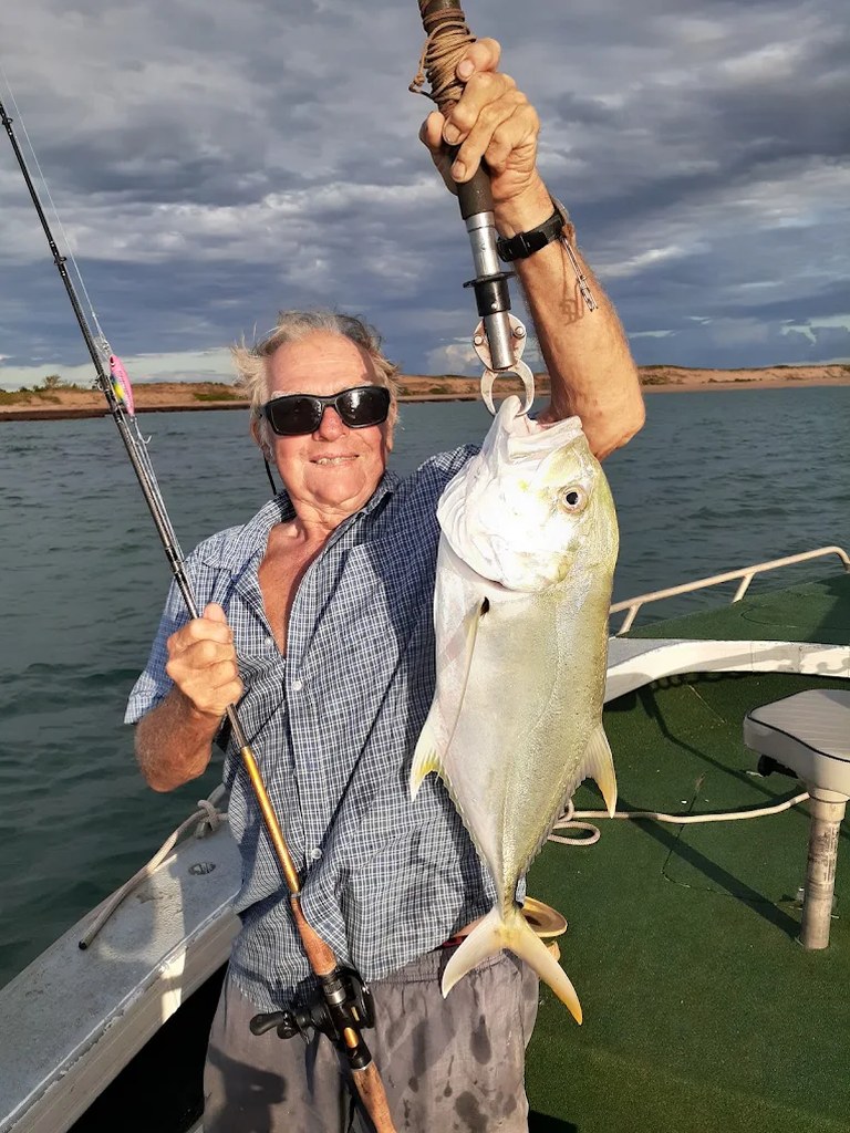 Angler on board holding a golden trevally at sunset